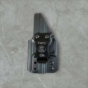 K&ouml;nnte beinhalten: Eine schwarze Polymerholster mit einem Metallclip. Auf dem Clip steht das Wort "Carry", das Gayle Force Tactical-Logo und das Wort "On". Die Holster hat mehrere Schraubenl&ouml;cher und ist f&uuml;r eine Schusswaffe konzipiert.