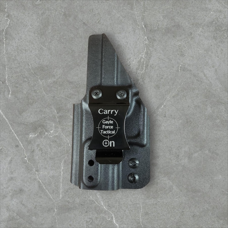 K&ouml;nnte beinhalten: Eine schwarze Polymerholster mit einem Metallclip. Auf dem Clip steht das Wort "Carry", das Gayle Force Tactical-Logo und das Wort "On". Die Holster hat mehrere Schraubenl&ouml;cher und ist f&uuml;r eine Schusswaffe konzipiert.