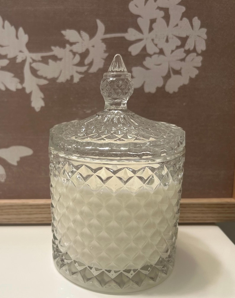 May include: A clear glass candle jar with a diamond pattern and a decorative lid. The jar is filled with a white candle. The candle jar is a decorative home decor item.