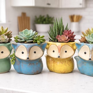 May include: A white ceramic mug with a black handle and the text "But First, Coffee" in a bold, black font. The mug is set against a blurred background, suggesting a cozy setting.