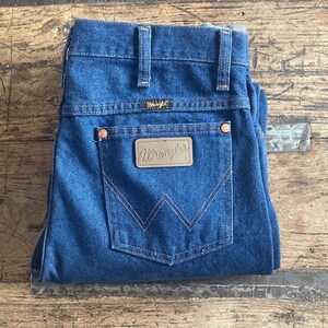 Może przedstawiać: Granatowe dżinsy Wrangler. Jeansy mają klasyczny design z pięcioma kieszeniami, z brązową sk&oacute;rzaną naszywką na tylnej kieszeni z logo Wrangler. Jeansy są starannie złożone, prezentując szczeg&oacute;ły szw&oacute;w i charakterystyczne "W" marki.