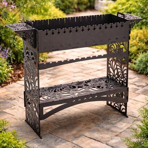 Op de afbeelding: Een zwarte metalen buitenbarbecue met decoratieve uitgesneden patronen. De barbecue heeft een rechthoekige vuurbox met sleuven voor spiesjes, een onderste plank en zijhandgrepen. De bloemmotieven geven een stijlvol element.