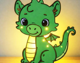 Può includere: Una luce notturna a forma di drago verde con un contorno marrone chiaro e un bagliore giallo. Il drago ha un viso sorridente con occhi grandi e una coda arricciata.