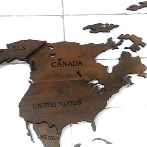 May include: A wooden map of North America, with the countries of U.S., Canada, United States, and Mexico labeled. The map is a dark brown color and is set against a white background.