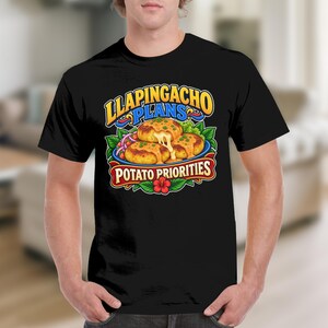 May include: A black short-sleeve t-shirt featuring a colorful graphic of llapingachos with melted cheese. The text reads LLAPINGACHO PLANS and POTATO PRIORITIES in bold yellow and white lettering, accented by green leaves and a red hibiscus flower.