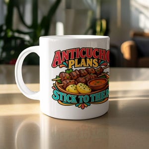 May include: A white ceramic mug featuring a colorful graphic of anticuchos on skewers with potatoes and a small bowl of sauce. The text reads "ANTICUCHO PLANS STICK TO THEM" in bold, stylized lettering with decorative flourishes in red, yellow, and teal.