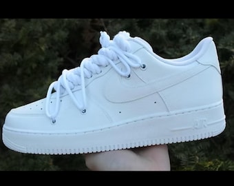 May include: A white leather trainer with a classic design. Features include a visible Nike swoosh, white laces, and the word "AIR" on the side. The shoe has a clean, minimalist aesthetic, suitable for casual wear.