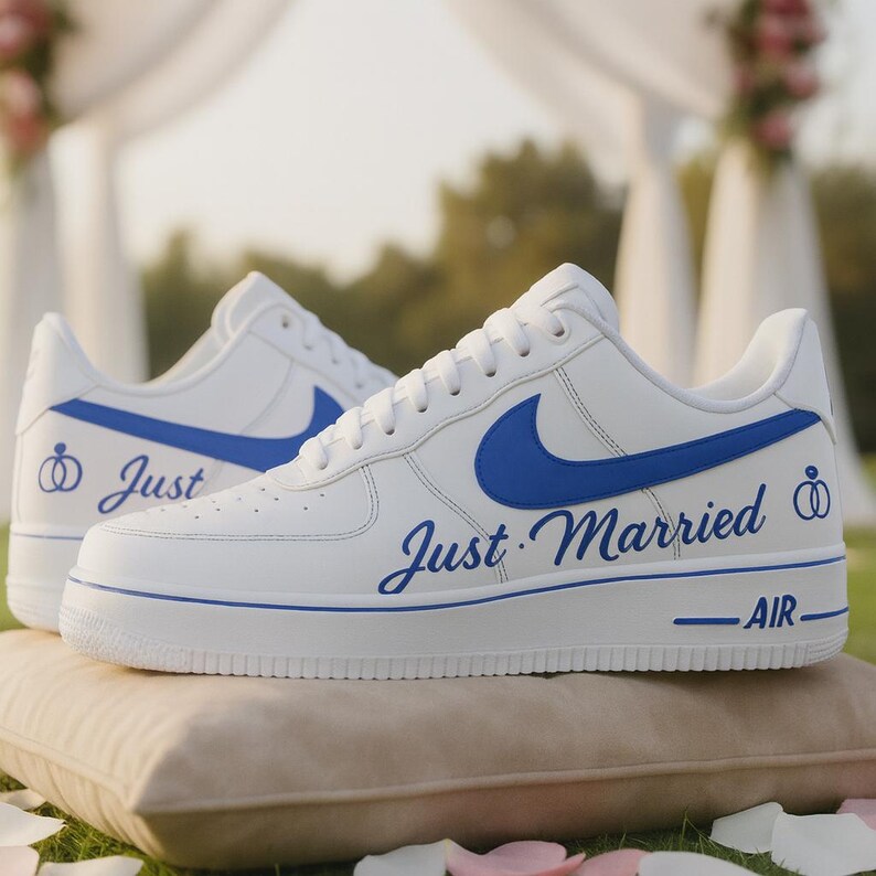 May include: White sneakers with blue accents, featuring the words "Just Married" in script. The shoes have a blue Nike swoosh and a wedding ring graphic. The word "AIR" is printed on the sole.