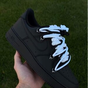 K&ouml;nnte beinhalten: Schwarze Nike Air Force 1 "Black Panda" Sneaker mit wei&szlig;en Schn&uuml;rsenkeln. Die Schuhe sind ganz schwarz mit einem wei&szlig;-schwarzen Schn&uuml;rsenkeldesign. Der Text "AF1 "BLACK PANDA"" befindet sich oben im Bild.