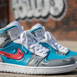 May include: A pair of high-top sneakers in a vibrant color scheme. The shoes feature a combination of blue, gray, red, and white. The design includes a red swoosh, white laces, and a gray and white sole. The sneakers have a unique, artistic style.