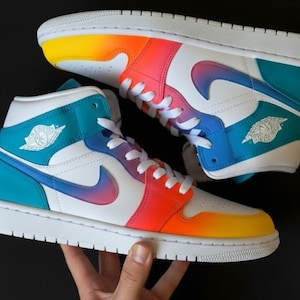May include: A pair of high-top sneakers with a vibrant color scheme. The shoes feature white, teal, orange, pink, and yellow accents. The iconic swoosh logo is visible on the side, and the shoes have white laces and soles.