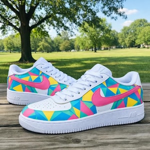 May include: White sneakers with a colorful geometric design. The shoes feature a pink swoosh and accents of blue, yellow, and green. The word "AIR" is visible on the sole.