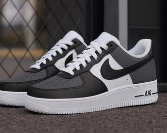 May include: Pair of gray, black, and white sneakers with white laces and a white sole. The sneakers have a black swoosh logo on the side and the word "AIR" printed on the midsole. The shoes are on a gray surface.