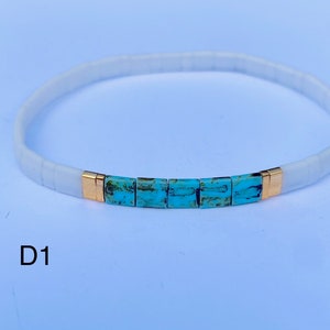 May include: White and turquoise beaded bracelet with gold accents. The bracelet has a simple design and is perfect for everyday wear.