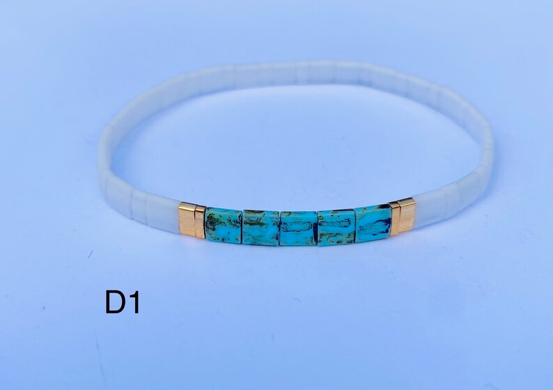 May include: White and turquoise beaded bracelet with gold accents. The bracelet has a simple design and is perfect for everyday wear.