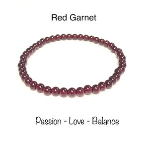 May include: Red Garnet bracelet made with small, dark red beads. The bracelet is on a white background. The text "Red Garnet" and "Passion - Love - Balance" is below the bracelet.