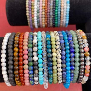 May include: A collection of colorful beaded bracelets, including black lava rock, tiger's eye, rose quartz, turquoise, and lapis lazuli.