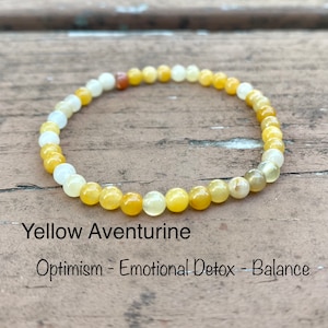 May include: A yellow aventurine beaded bracelet. The bracelet is made of small, round, yellow beads with a few white and brown beads. Text on the image reads "Yellow Aventurine" and "Optimism - Emotional Detox - Balance."