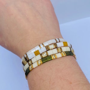 May include: A set of three bracelets stacked on a wrist. The bracelets are made of white, gold, and green tiles. The tiles are arranged in a pattern.