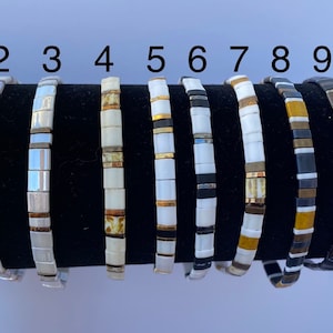 May include: Ten different bracelets with various color combinations of white, gold, black, and iridescent beads. The bracelets are numbered 1 through 10 and labeled with the letter A.