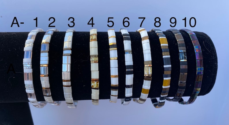May include: Ten different bracelets with various color combinations of white, gold, black, and iridescent beads. The bracelets are numbered 1 through 10 and labeled with the letter A.