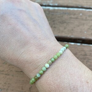 May include: A green and white gemstone bracelet with round beads. The bracelet is on a person's wrist.