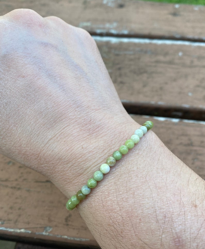May include: A green and white gemstone bracelet with round beads. The bracelet is on a person's wrist.