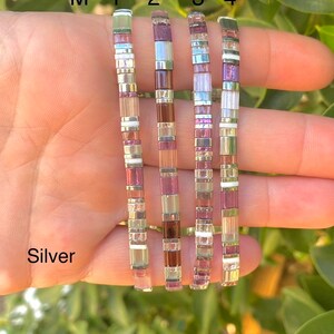 May include: Five silver bracelets with different colored beads. The bracelets are labeled M-1, 2, 3, and 4. The beads are in shades of purple, pink, and white.