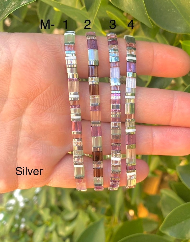 May include: Five silver bracelets with different colored beads. The bracelets are labeled M-1, 2, 3, and 4. The beads are in shades of purple, pink, and white.