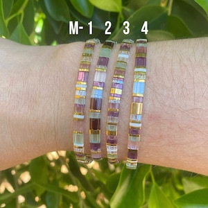 May include: Five colorful bracelets with a mix of purple, white, and gold beads. The bracelets are labeled M-1, 2, 3, and 4.