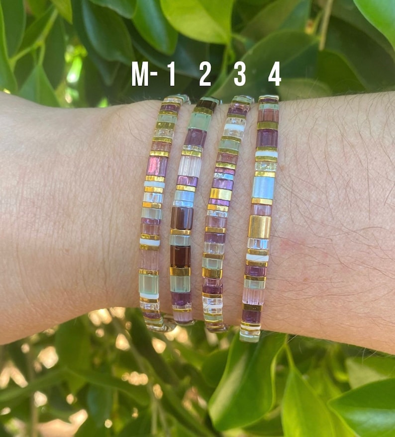May include: Five colorful bracelets with a mix of purple, white, and gold beads. The bracelets are labeled M-1, 2, 3, and 4.