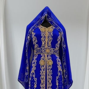 May include: A royal blue caftan-style dress with gold embroidery and embellishments. The dress features a hood and a matching belt. The intricate design includes floral and geometric patterns, creating an elegant look.