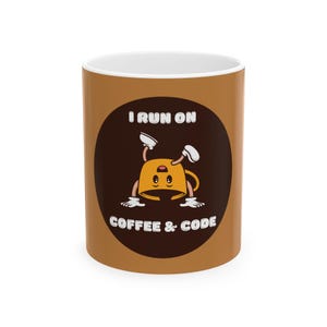 May include: A brown ceramic coffee mug with a black circle design. The circle features a cartoon coffee cup with a face and arms, doing a handstand. The text "I run on coffee & code" is printed below the cartoon.