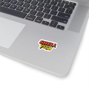 Könnte beinhalten: Ein Aufkleber mit dem Text "SHELL YEAH" in roten und gelben Buchstaben auf weißem Hintergrund.