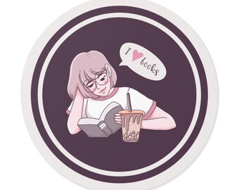 May include: Round sticker featuring a cartoon illustration of a person reading a book and drinking a beverage. The person is wearing glasses and a white shirt with pink trim. A speech bubble says "I ❤️ books."