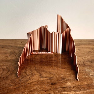 May include: A wooden model of Mount Kilimanjaro, a mountain in Tanzania, with a label that reads "Mt. Kilimanjaro". The model is made of thin strips of wood that are arranged to create the shape of the mountain.