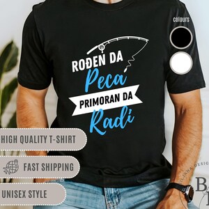 May include: Black t-shirt with a blue graphic of a fishing rod and the text "ROĐEN DA Peca PRIMORAN DA Radi". The shirt is available in black and white.