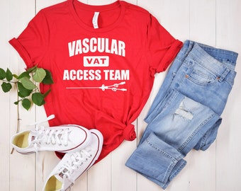 May include: Red t-shirt with white text that reads "Vascular VAT Access Team". The shirt is paired with blue jeans and white sneakers.