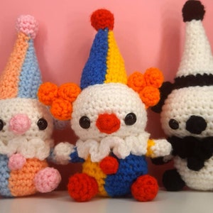 May include: Three handmade crochet clown dolls. The clowns have white bodies, colorful hats, and orange hair. One clown has a blue, yellow, and red hat, another has a blue, orange, and pink hat, and the third has a black and white hat.