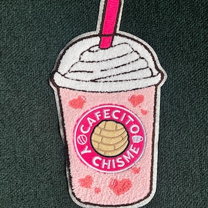 May include: Pink and white embroidered patch of a coffee drink with whipped cream and a pink straw. The drink has a pink circle with the text "Y Cafecito Y Chismes" in white.
