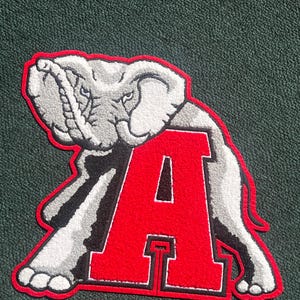 May include: A large, embroidered patch featuring a gray elephant and a bold red letter "A". The elephant is detailed with white accents and a black outline, set against a dark green background. The letter "A" has a white border.
