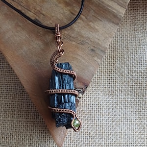 Raw Tourmaline snake pendant, handcrafted using antiqued copper wire, with a faceted peridot bead.