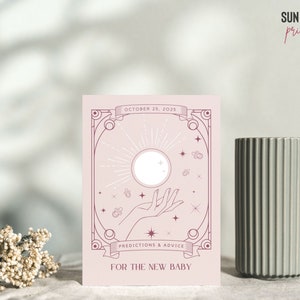 May include: A light pink card with a celestial design featuring a sun, hand, and stars. The text reads "October 25, 2025" and "Predictions & Advice For The New Baby". A gray ribbed vase is to the right.