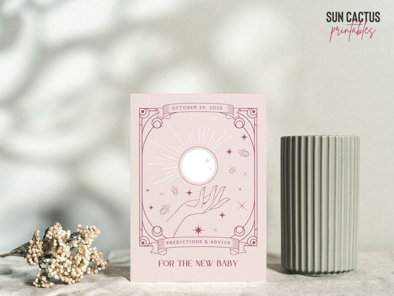 May include: A light pink card with a celestial design featuring a sun, hand, and stars. The text reads "October 25, 2025" and "Predictions & Advice For The New Baby". A gray ribbed vase is to the right.