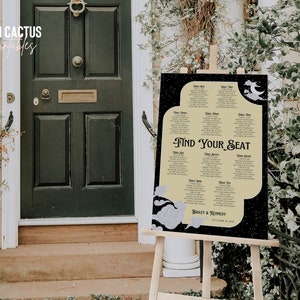 May include: A wedding seating chart on an easel. The sign has a black background with a cream-colored center, featuring the text "Find Your Seat." The names of the guests are listed below the text.