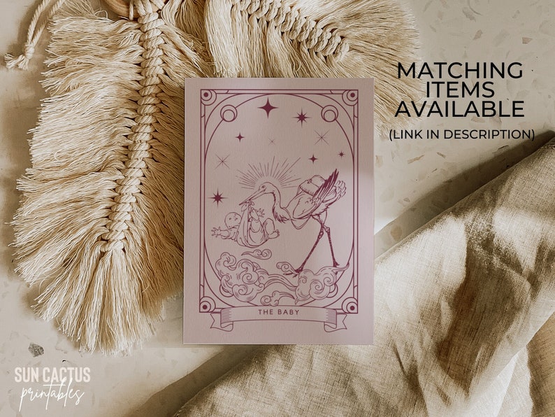 May include: A mauve-colored print featuring a stork carrying a baby, with the text "THE BABY" on a banner. The print has an art deco style with stars and decorative borders. Text on the print says "MATCHING ITEMS AVAILABLE (LINK IN DESCRIPTION)".