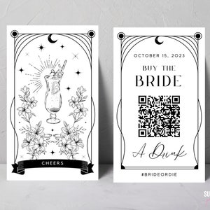 May include: Two black and white art deco style prints. One features a cocktail illustration, flowers, stars, and a banner with "Cheers." The other says "Buy the Bride A Drink" with a QR code and the date October 15, 2023.