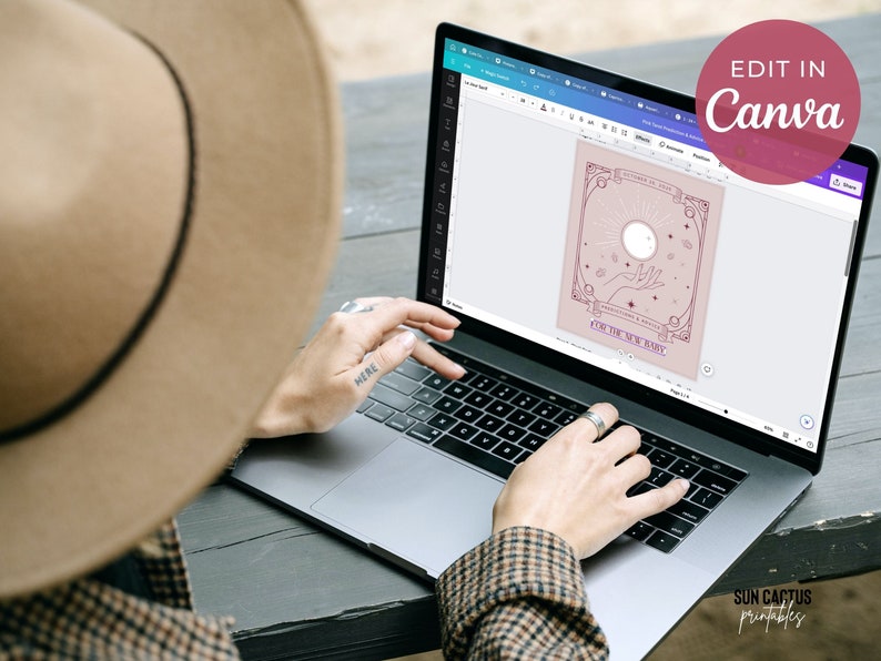 May include: A laptop displaying a digital design with a celestial theme, featuring a sun, hand, and stars, with the text "EDIT IN Canva" in a pink circle. The design includes the text "FOR THE NEW BABY".
