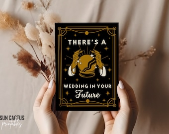May include: A black card with gold accents and the text "THERE'S A WEDDING IN YOUR FUTURE". The card features a gold crystal ball with hands and stars. The Sun Cactus Printables logo is in the bottom left corner.