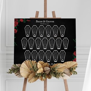 Puede incluir: Un plano de asientos de boda negro con asignaciones de mesa en forma de ata&uacute;d blanco, cada una con una calavera. Las palabras "Bride & Groom" y la fecha est&aacute;n en la parte superior. Rosas rojas y vegetaci&oacute;n decoran las esquinas.